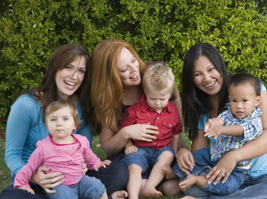 Zwei Frauen mit drei Kindern sitzen lachend im Grünen